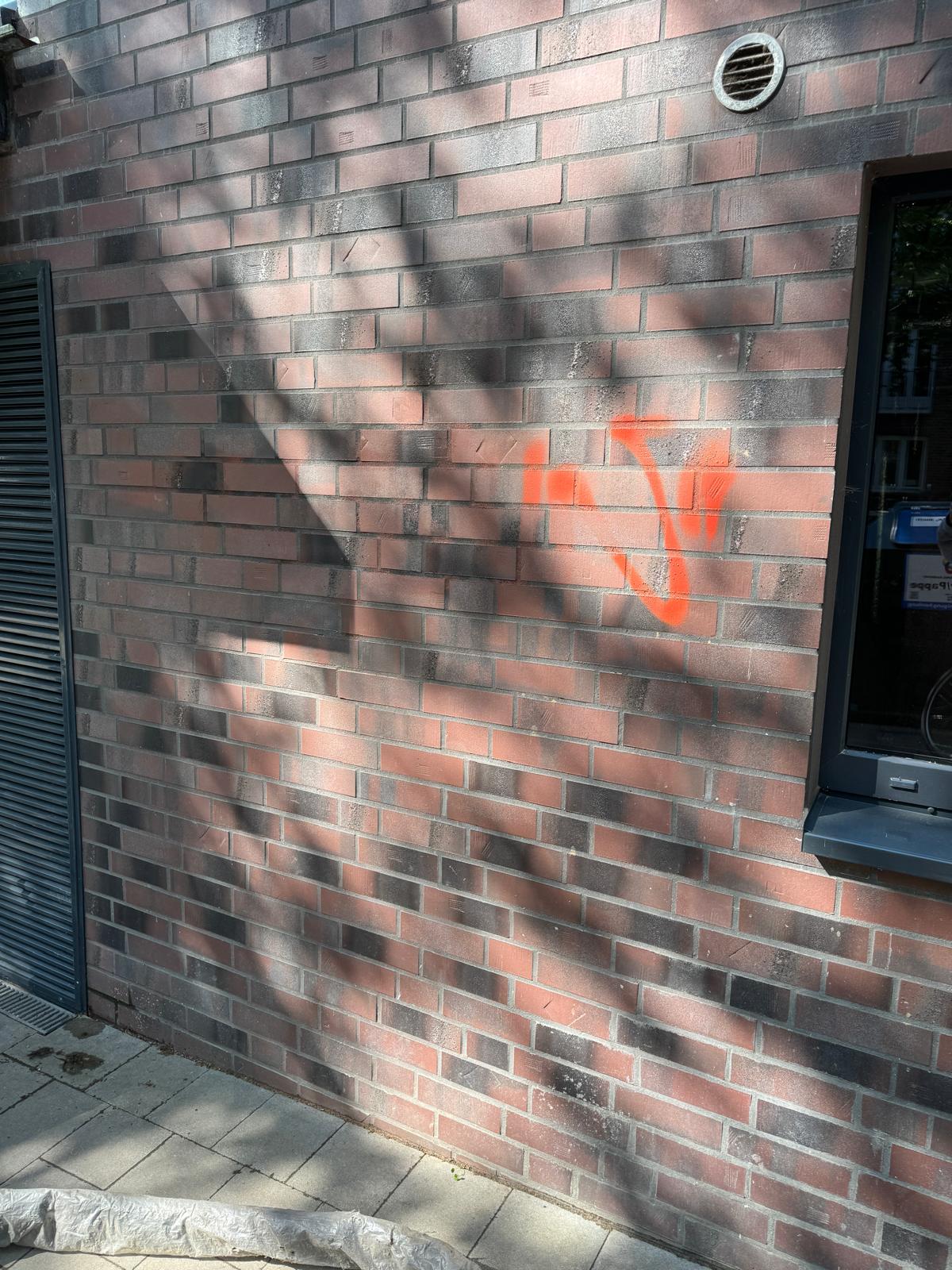 Rotes Graffiti auf einer dunklen Klinkerfassade